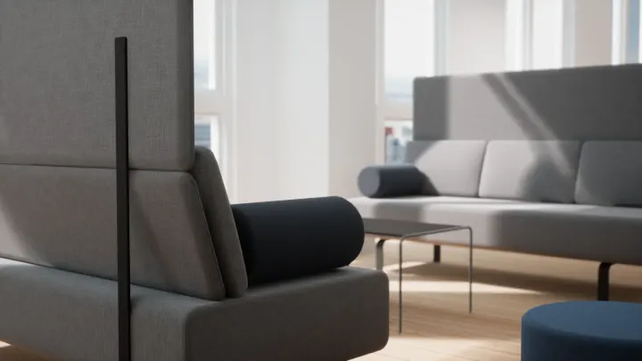 Nahaufnahme grauer Loungesofas mit einer dunklen Nackenrolle, einem niedrigen Tisch und einem blauen Hocker im Sonnenlicht